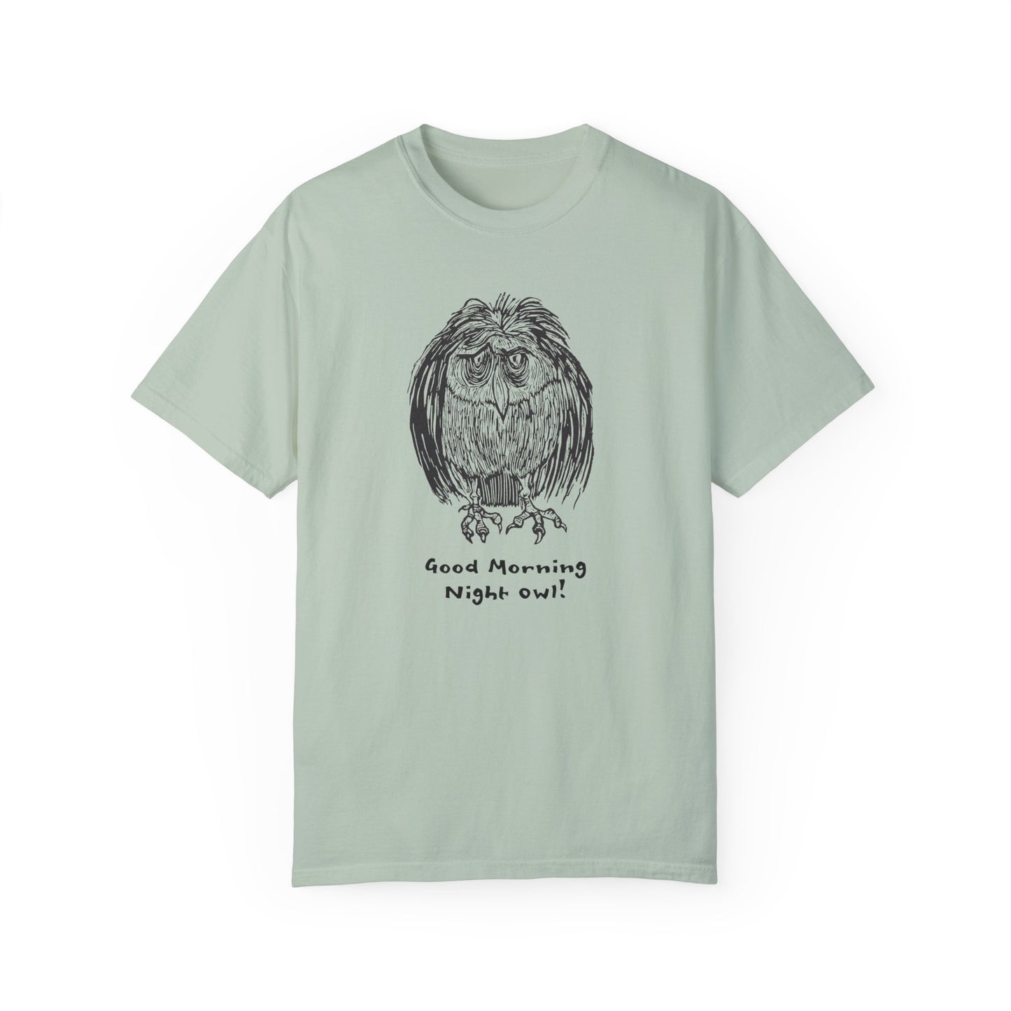 Alt text: Light green or sage colored t-shirt featuring an illustration of a tired-looking owl with messy feathers, created from a linoleum block print. The owl stands with drooping eyes, and below it, the text reads: “Good Morning Night Owl!