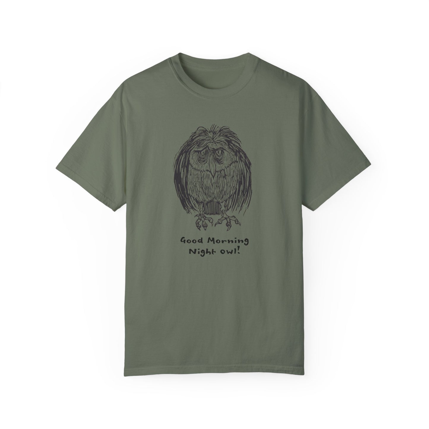 Dark green or moss green colored t-shirt featuring an illustration of a tired-looking owl with messy feathers, created from a linoleum block print. The owl stands with drooping eyes, and below it, the text reads: “Good Morning Night Owl!