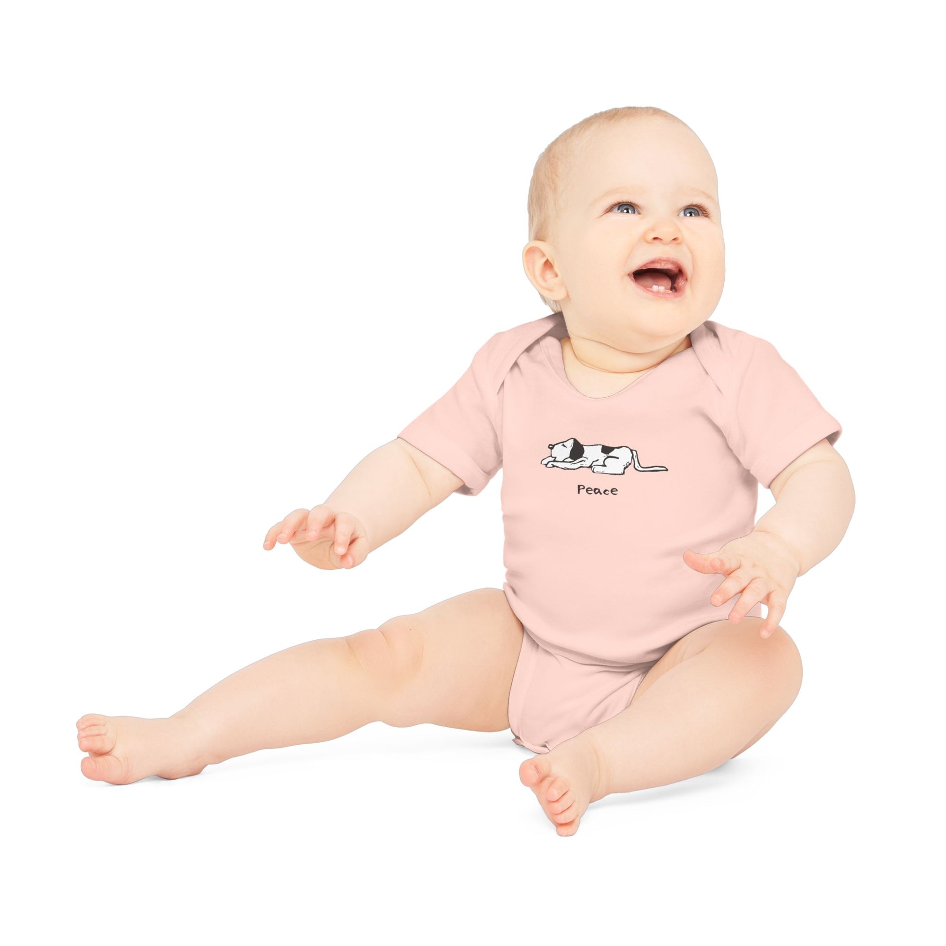 Light pink short sleeve onesie baby bodysuit on a smiling baby sitting up with arm outstretched in front, with head turned and looing up. Onesie features a simple black and white illustration of a sleeping dog above the word "Peace" printed on the chest.