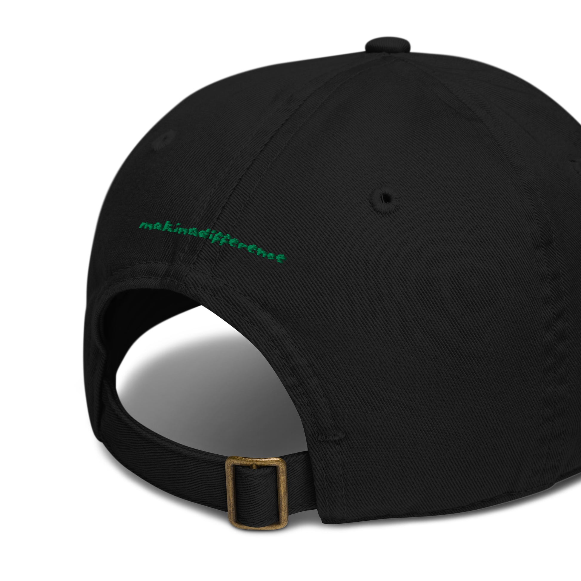 Rear view of a black baseball cap featuring an adjustable brass buckle strap and small green embroidered text that reads "makinadifference" above the opening.