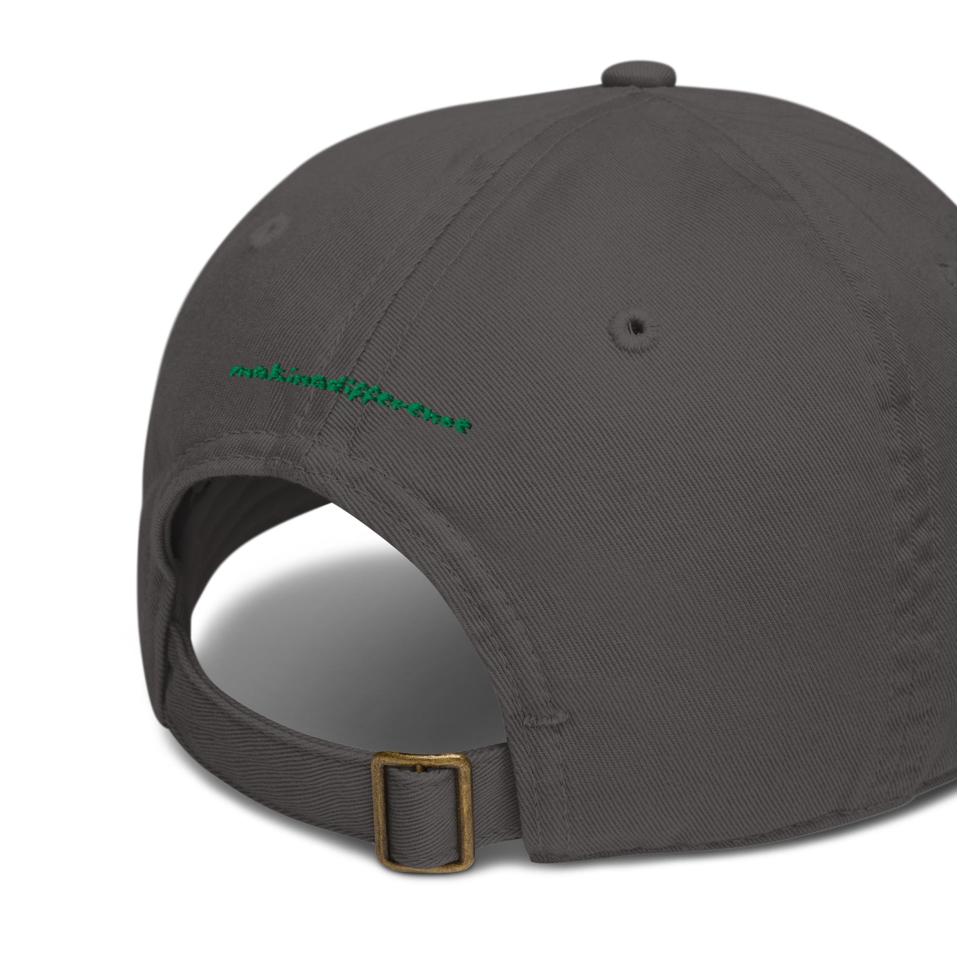 Rear view of a charcoal colored baseball cap featuring an adjustable brass buckle strap and small green embroidered text that reads "makinadifference" above the opening.