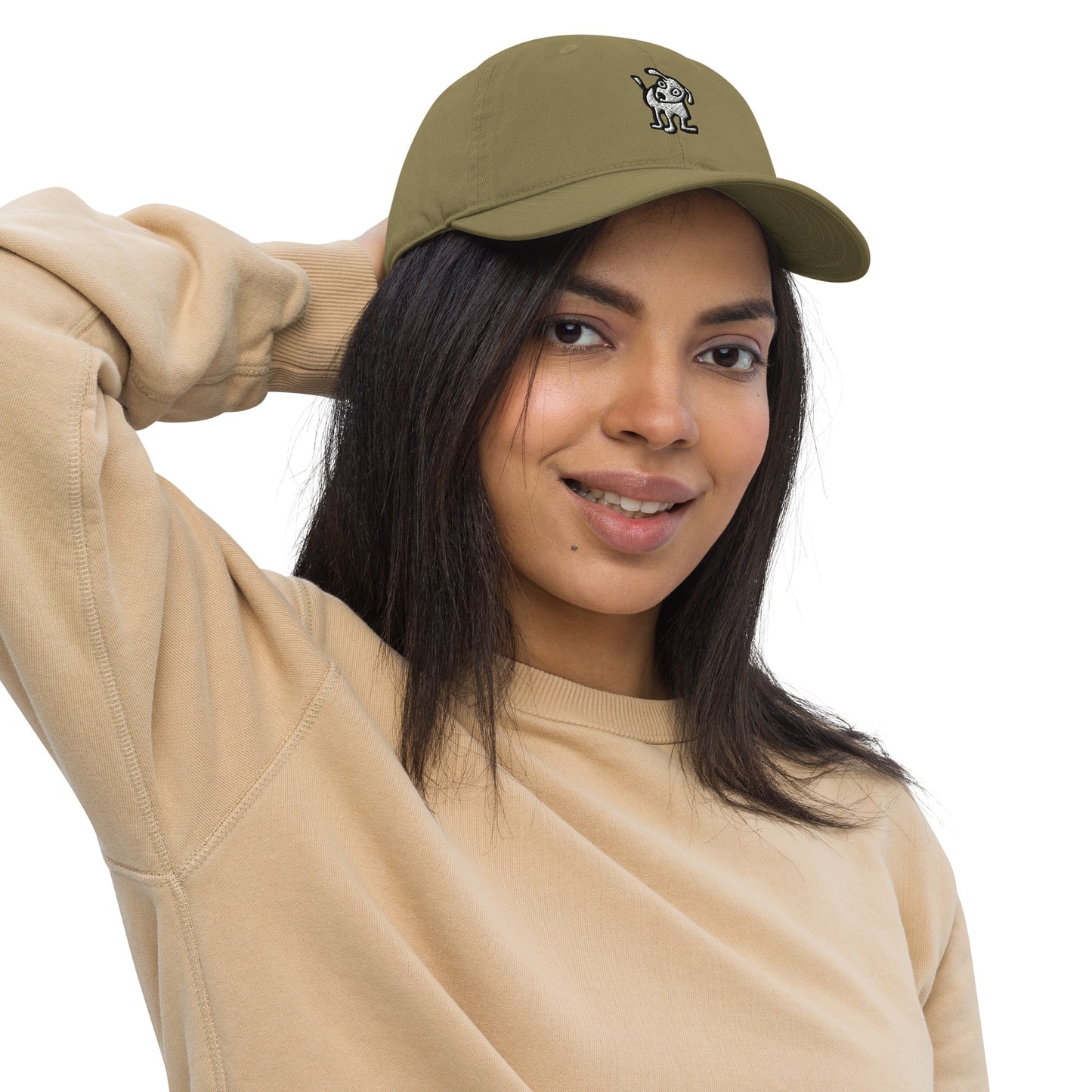Woman wearing a jungle green baseball cap with an embroidered cartoon-style dog logo on the front, smiling and posing with one hand resting on the back of her head; she is dressed in a beige sweatshirt and has long, dark hair.